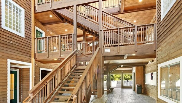 Un interior de madera de varios niveles con una escalera central, suelo de piedra y grandes ventanales.
