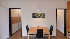 Ruokailutilassa on puinen pöytä, mustat tuolit, valkoinen riippuvalaisin ja seinällä oleva kehystetty taulu.