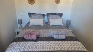 Ein ordentlich bezogenes Bett mit gemusterten Betttextilien und zwei Kissen, eine Nachttischlampe und Wanddekor.