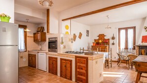 A kitchen with a central island, wooden cabinets, a built-in oven, and a dining area with wicker chairs. - Country House - Isola dei Cavalli (Manziana)