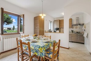 A dining area with a table set for four, a window with a view, and a kitchen in the background. - House Tiziana Close by Mare Argentario (Manciano)