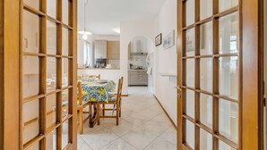 A dining area with a table set for four, a kitchen in the background, and a hallway leading to a door with glass panels. - House Tiziana Close by Mare Argentario (Manciano)