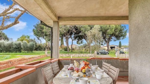 An outdoor dining area with a table set for four, surrounded by a concrete wall and wooden benches. - House Tiziana Close by Mare Argentario (Manciano)