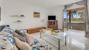 A living room with a sofa, glass coffee table, TV, wooden cabinet, and a door leading to a balcony. - House Tiziana Close by Mare Argentario (Manciano)