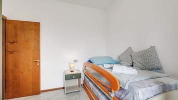 Un dormitorio con una puerta de madera, una mesita de noche con lámpara, una cama con almohadas y una cómoda.