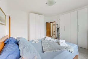 A bedroom with a bed, pillows, a blanket, and a folded towel. There is a wooden door and a white wardrobe. - House Tiziana Close by Mare Argentario (Manciano)