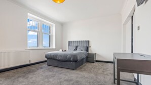 A bedroom with a bed, bedside tables, a desk, a window, and a radiator. - Eden View Jungle Room (Lake District)