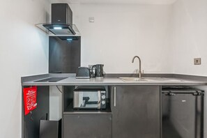 A compact kitchenette with a microwave, coffee maker, and sink.