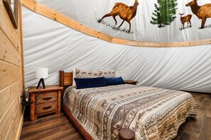 A tent-style room with a bed, a nightstand, a lamp, and a wall with animal prints. - Arrowhead Tepee | Near Dollywood | Resort Access (Sevierville)