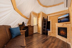 A tent with a wooden interior, a fireplace, a television, and a ladder.