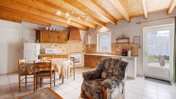 A cozy kitchen with wooden beams, a dining area with a table and chairs, and a patterned armchair.