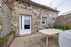 Ein Steinhaus mit weißer Tür, einem kleinen Fenster und einem Tisch mit weißem Tischtuch.