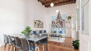 Een eethoek met een houten vloer, een marmeren tafel en zwarte stoelen. Er is een bank met blauwe kussens en een schilderij van een gebouw aan de muur.