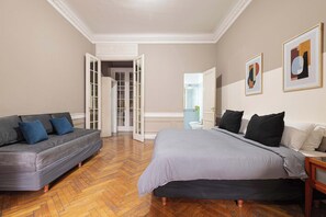 A bedroom with a bed, a sofa, a door leading to another room, and a wall with framed artwork. - LDV Aparts 2B by MOT Rentals (Buenos Aires)