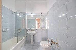 A bathroom with a bathtub, sink, and toilet, featuring a glass shower enclosure and tiled walls. - LDV Aparts 2B by MOT Rentals (Buenos Aires)