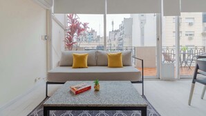 Ein Balkon mit einer Couch, einem Tisch mit einer Schachtel und einer Pflanze, und Blick auf Gebäude.