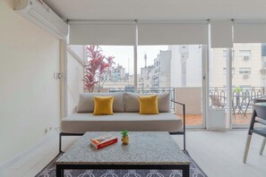 A balcony with a sofa, a table with a box and a plant, and a view of buildings. - LDV Aparts 5A by MOT Rentals (Buenos Aires)