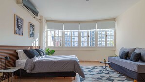 Een slaapkamer met een bed, een bank, een bijzettafeltje, een plant en grote ramen.