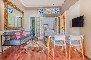A modern living room with a sofa, a dining table with chairs, a large mirror, and a kitchen visible through an open door. - LDV Aparts 3B by MOT Rentals (Buenos Aires)