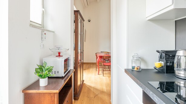 Una cocina con microondas, cafetera y un comedor con sillas y una mesa.