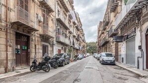 Una calle estrecha flanqueada por edificios de varios pisos, coches estacionados y una motocicleta.