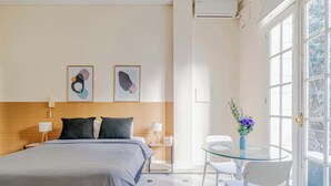 Een moderne hotelkamer met een bed, nachtkastjes, een glazen tafel met stoelen en kunst aan de muur.