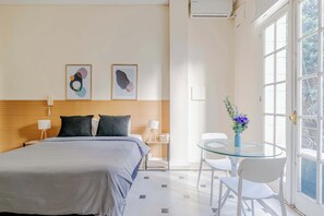 Ein modernes Hotelzimmer mit Bett, Nachttischen, einem Glastisch mit Stühlen und einem Kunstwerk an der Wand.