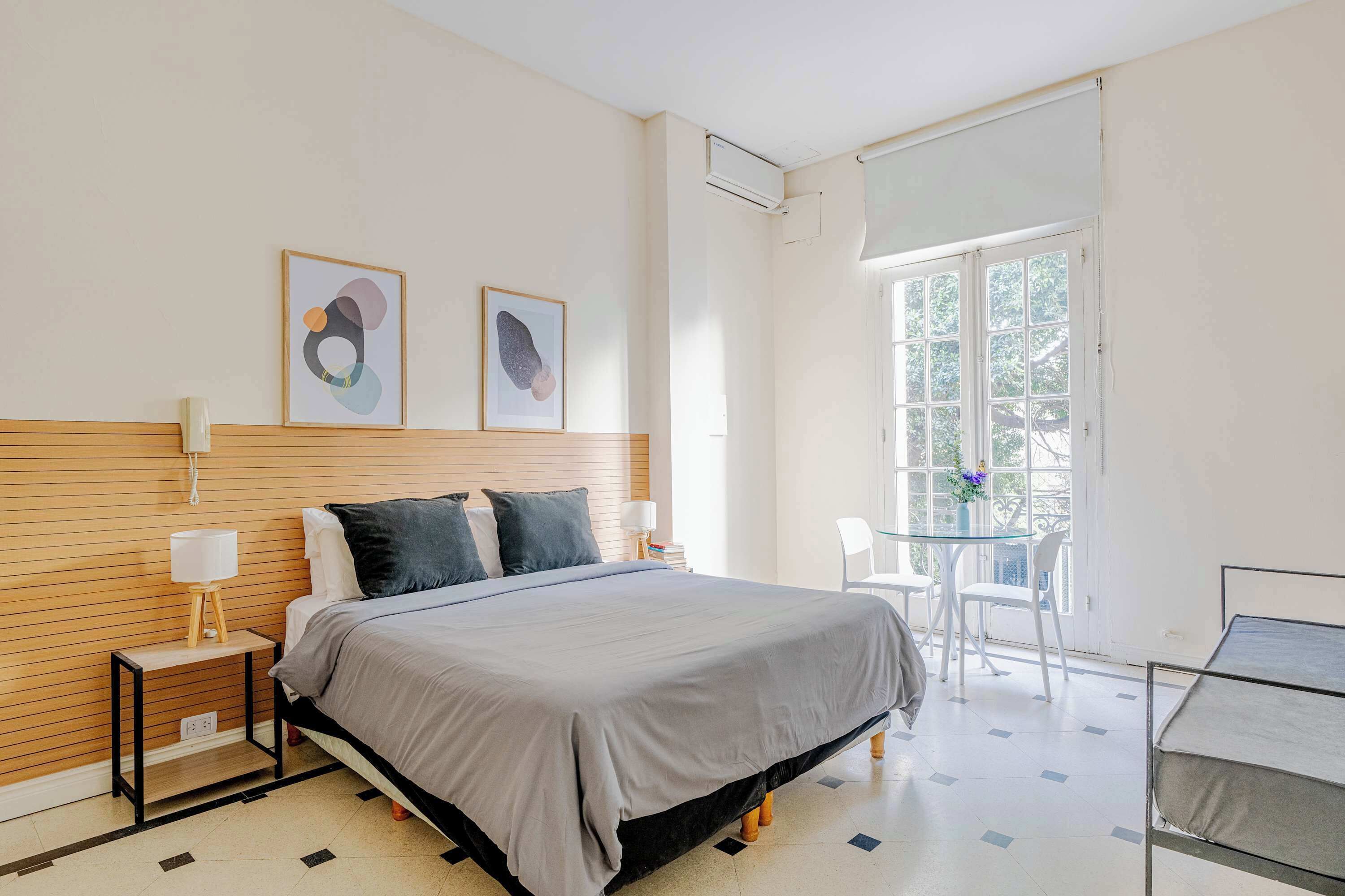 A modern bedroom with a bed, bedside tables, a window with a view, and a balcony with chairs.