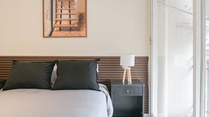 Une chambre à coucher avec un lit, des oreillers, une table de chevet, une lampe, un miroir et une porte.