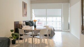 Un salon moderne avec une table à manger ronde, des chaises blanches, un canapé, une plante en pot et une grande fenêtre donnant sur un beau paysage.