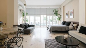 Una moderna camera d'albergo con zona pranzo, divano, letto e un'ampia finestra che si affaccia sull'esterno.