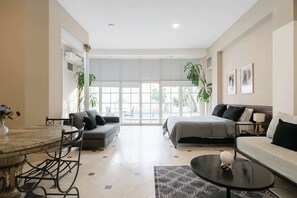 Une chambre d’hôtel moderne dotée d’un coin repas, d’un canapé, d’un lit et d’une grande fenêtre donnant sur l’extérieur.