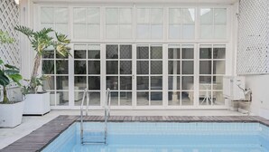 Una piscina con una scala in metallo, circondata da piante in vaso e un recinto bianco.