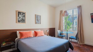 A hotel room with a bed, two framed pictures, a window with curtains, a table with chairs, and a small plant. - LDV Aparts 3A by MOT Rentals (Buenos Aires)