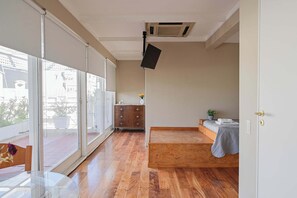 A room with a large sliding glass door, a wooden floor, a bed with a gray blanket, a small dresser, and a ceiling-mounted projector. - LDV Aparts 6A (Private Pool) by MOT Rentals (Buenos Aires)