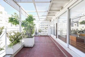A balcony with potted plants, a red tiled floor, and a view of buildings. - LDV Aparts 6A (Private Pool) by MOT Rentals (Buenos Aires)