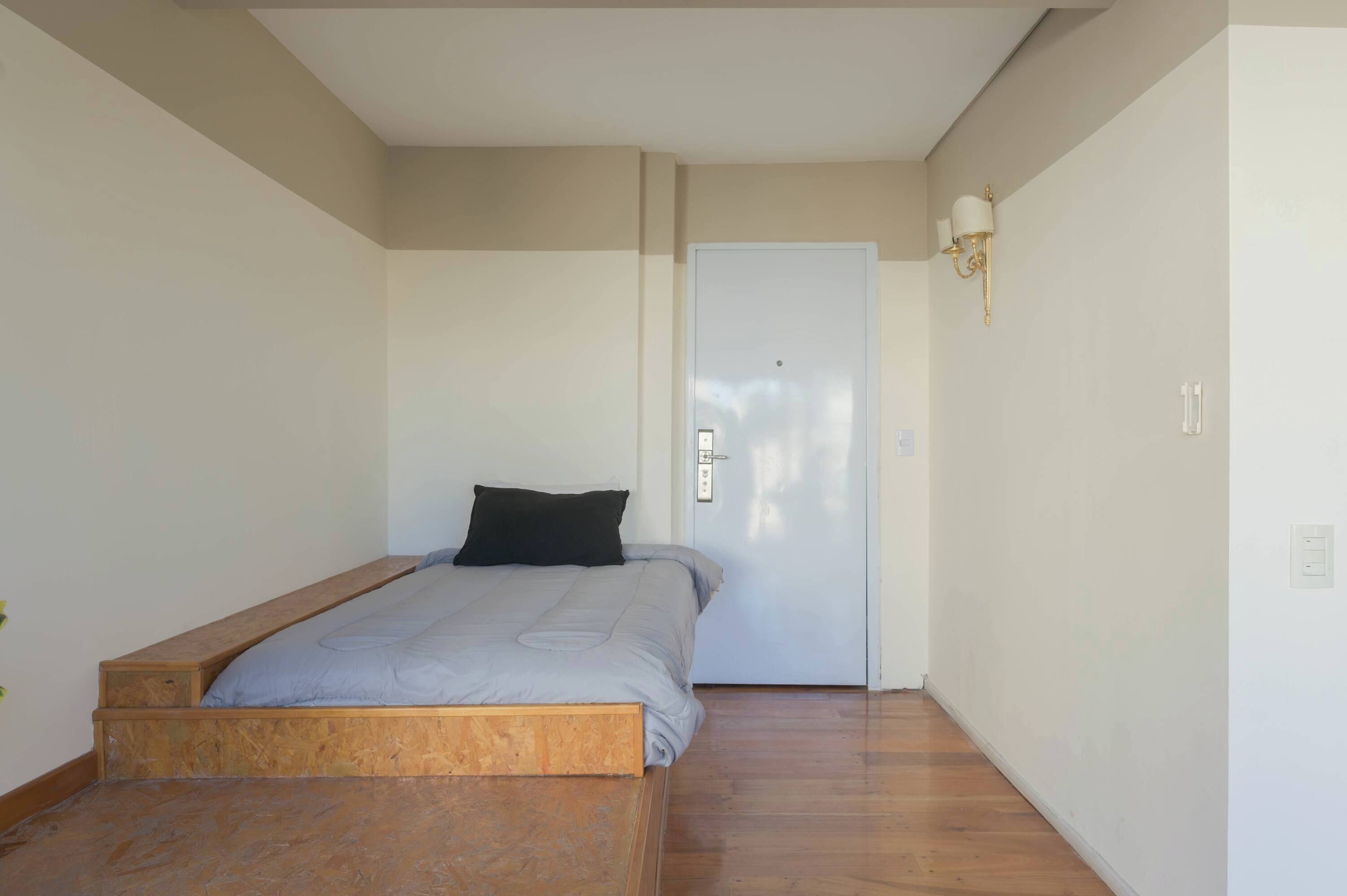 Une chambre avec un lit simple, une porte blanche et un luminaire fixé au mur.