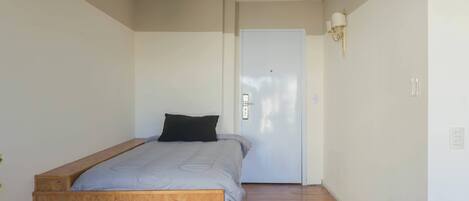 Une chambre avec un lit simple, une porte blanche et un luminaire fixé au mur.