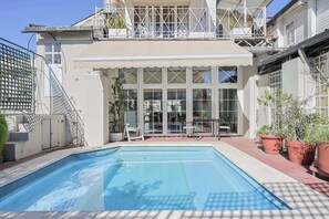 A pool with a covered patio area, a staircase, and a balcony with outdoor furniture. - LDV Aparts 6A (Private Pool) by MOT Rentals (Buenos Aires)