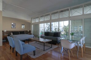 A modern living room with a sofa, chairs, a coffee table, and a bed. Large windows provide a view of the outside. - LDV Aparts 6A (Private Pool) by MOT Rentals (Buenos Aires)