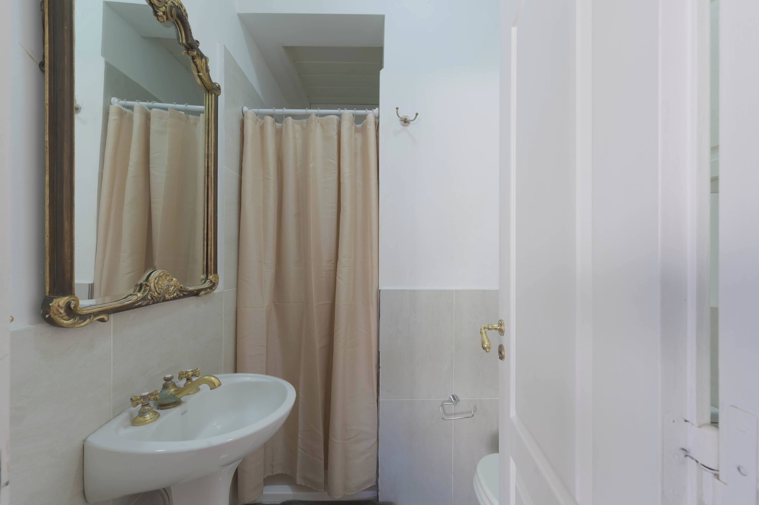 A bathroom with a white sink, a mirror with an ornate frame, a shower curtain, and a toilet.