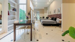 Ein modernes Hotelzimmer mit Essbereich, zwei Betten, einem großen Fenster und Blick auf Grünfläche.