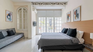 Un dormitorio con cama, sofá, ventana y una obra de arte en la pared.