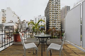 A balcony with a round table and two chairs, surrounded by potted plants and a view of city buildings. - LDV Aparts 4E by MOT Rentals (Buenos Aires)