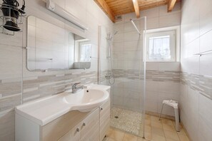 Een moderne badkamer met een grote spiegel, een wastafel, een douche en een klein krukje.