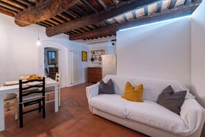 Ein Wohnzimmer mit einem weißen Sofa, einem Esstisch mit Stühlen, einer Küchenzeile mit Kühlschrank und einer rustikalen Decke.
