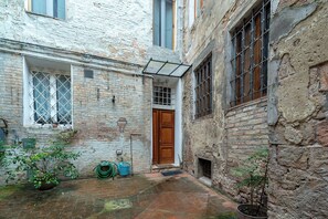 A narrow alleyway with a wooden door, a window with a metal grille, and a potted plant. - Cosy apartment for 4 people with WIFI and TV (Siena)