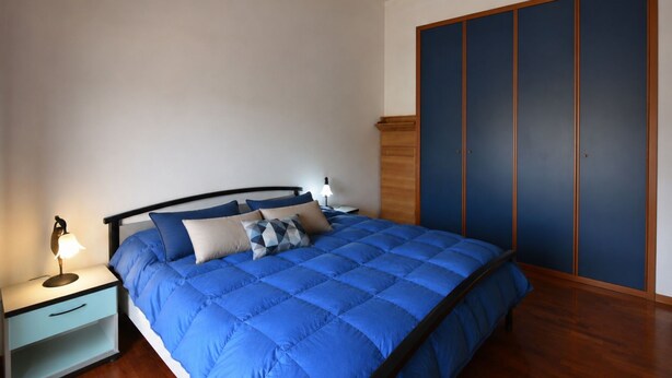 Um quarto com uma cama, mesa de cabeceira, abajur e guarda-roupa.
