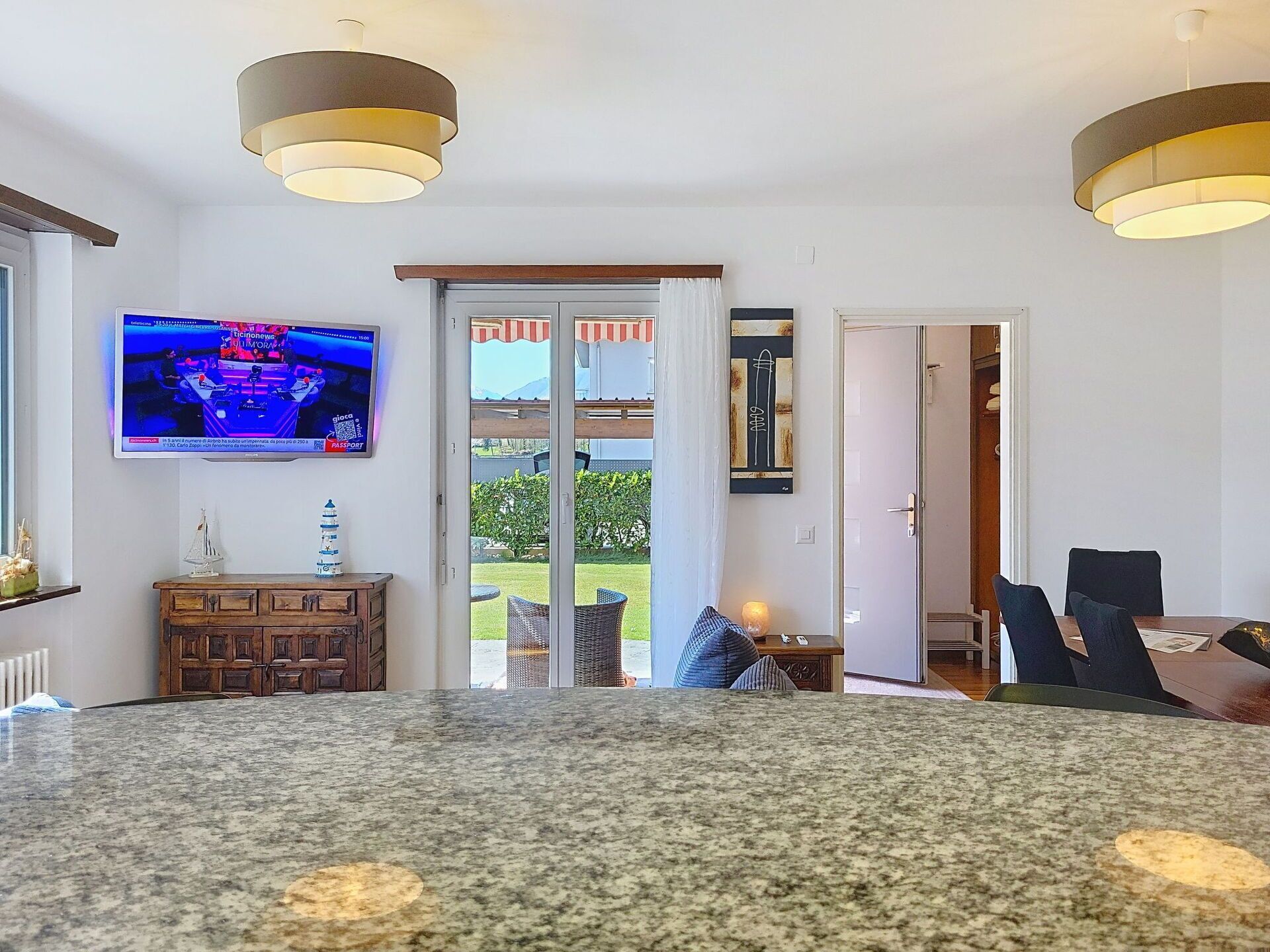 Un saló modern amb un ampli taulell de granat, una televisió penjada a la paret i una porta corredissa de vidre que dona a una zona exterior.