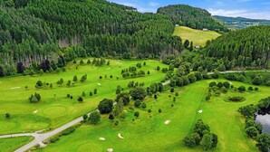 Un parcours de golf comportant plusieurs trous, entouré d’une forêt dense et de collines ondoyantes.